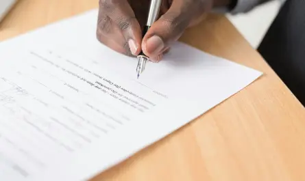 personne signant un document officiel sur un bureau en bois