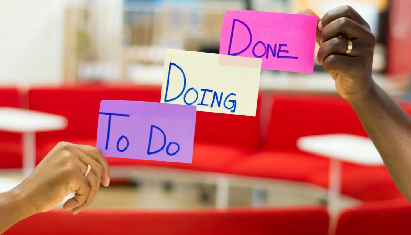 deux mains tenant des post-its colorés affichant "to do", "doing" et "done" illustrant la productivité