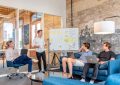 three men sitting while using laptops and watching man beside whiteboard