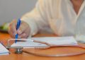 a person writing on a piece of paper with a stethoscope