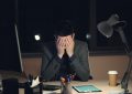 Man in suit sits at desk, head in hands.