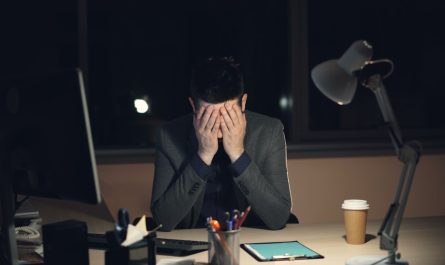 Man in suit sits at desk, head in hands.
