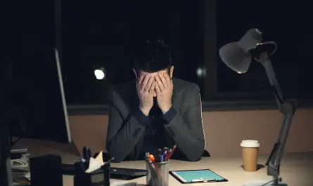 Man in suit sits at desk, head in hands.