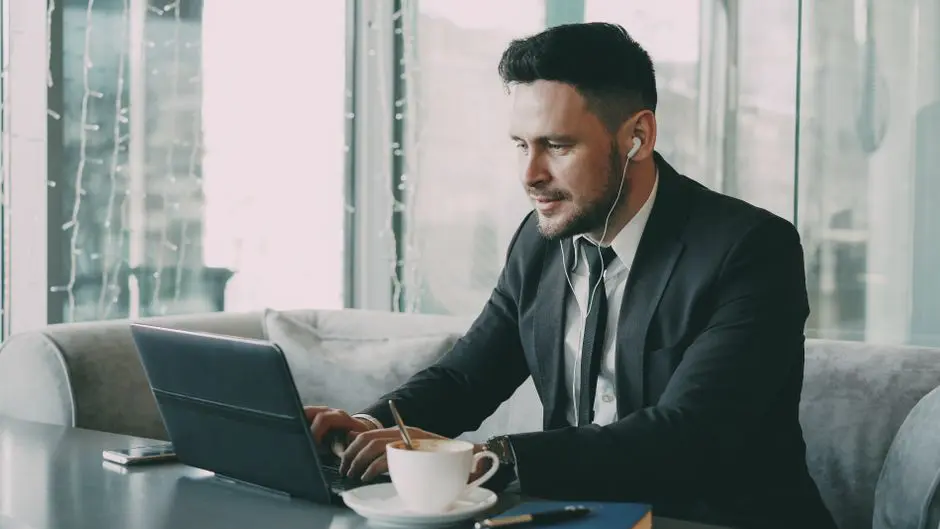 Business professional using a laptop in a cafe, wearing earbuds.