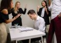 A team confronts a stressed colleague at a tense office meeting, highlighting workplace dynamics.