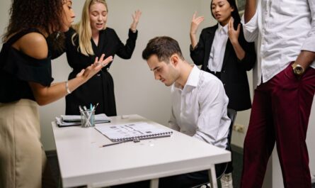 A team confronts a stressed colleague at a tense office meeting, highlighting workplace dynamics.
