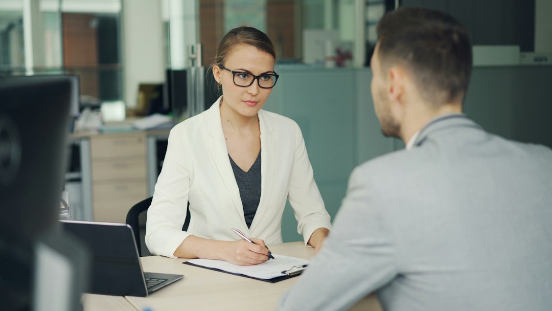 Woman in glasses interviews man at office desk