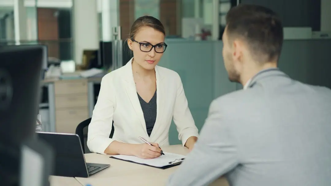 Woman in glasses interviews man at office desk